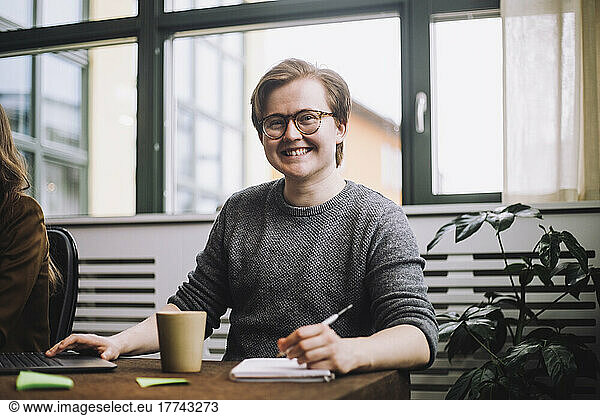 Portrait of happy young male entrepreneur wearing eyeglasses while sitting at conference table