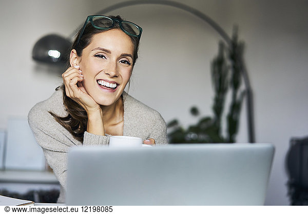 Portrait of happy young woman at home with laptop
