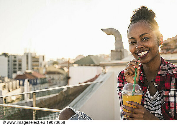 Portrait of happy young woman having a drink on rooftop at sunset