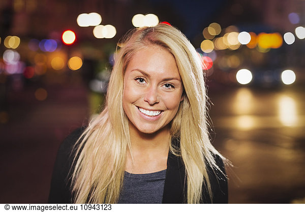 Portrait of happy young woman on city street at night