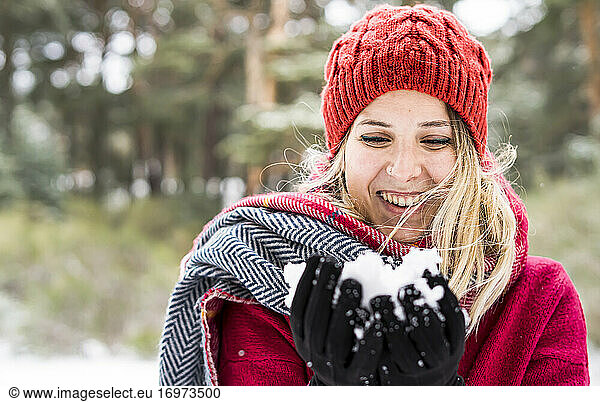 Portrait of happy young woman playing with snow in winter  blowing snowflakes to camera  copy space