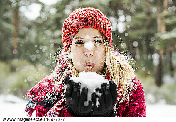Portrait of happy young woman playing with snow in winter  blowing snowflakes to camera  copy space