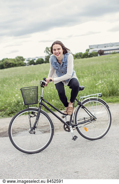 Portrait of happy young woman sitting on bicycle at countryside