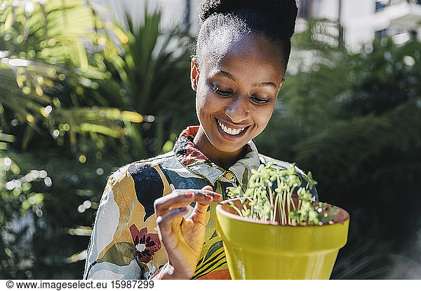 Portrait of happy young woman watching sprouts in flowerpot in garden