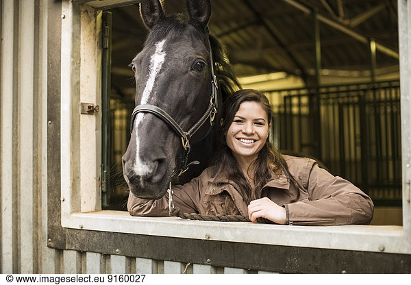 Portrait of happy young woman with horse in stable