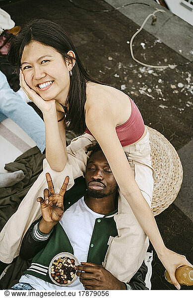 Portrait of happy young woman with male friend gesturing peace sign during rooftop party
