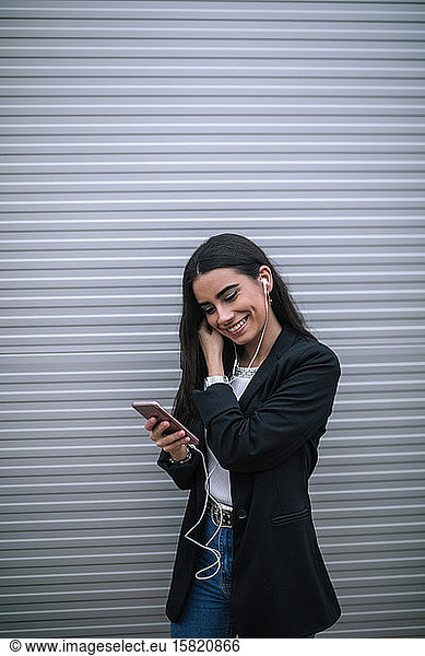 Portrait of happy young woman with smartphone putting on earphones