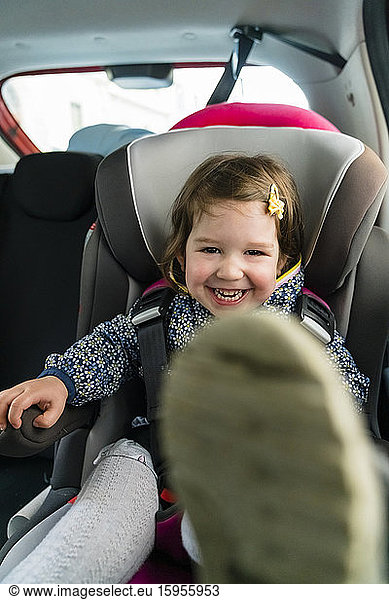 Portrait of laughing little girl sitting on child's seat in car