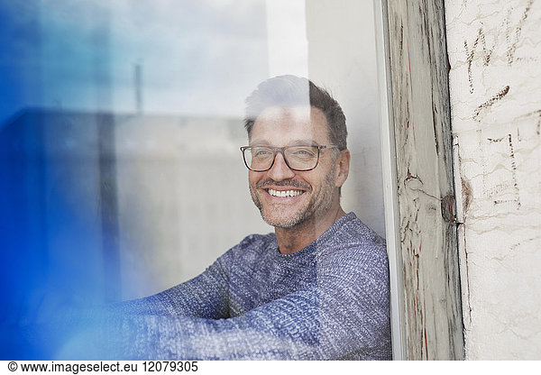 Portrait of laughing man behind glass pane wearing glasses