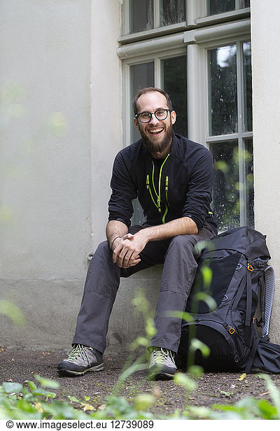 Portrait of laughing man with backpack waiting outdoors