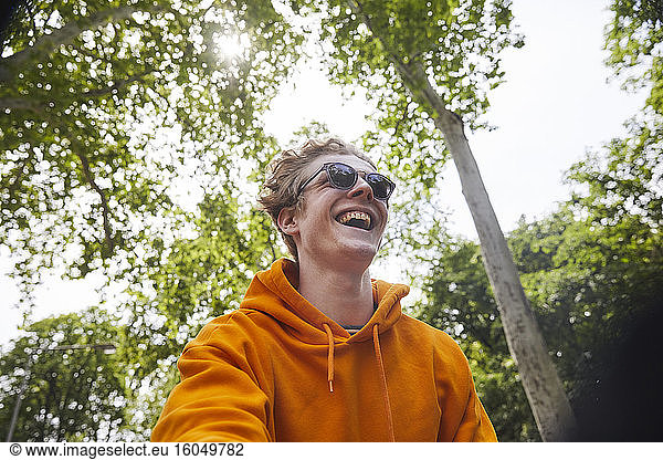Portrait of laughing young man wearing sunglasses and orange hoodie shirt in nature