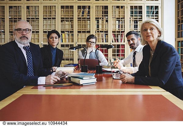 Portrait of lawyers sitting in board room against bookshelf
