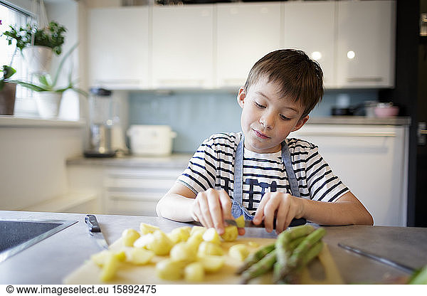 Portrait of little boy cutting potatoes in the kitchen