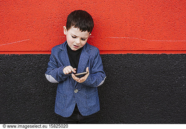 Portrait of little boy wearing suit coat using smartphone
