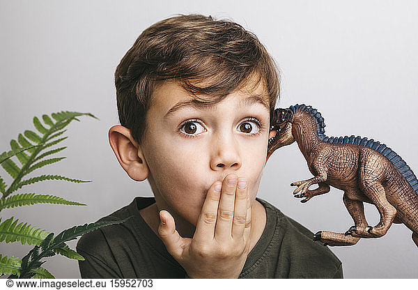 Portrait of little boy with toy dinosaur pulling funny face