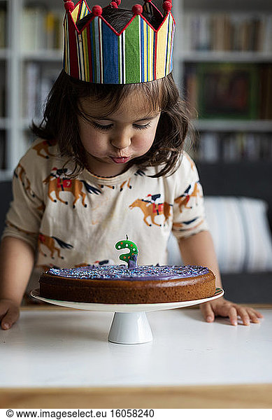 Portrait of little girl blowing out candle on her birthday cake at home