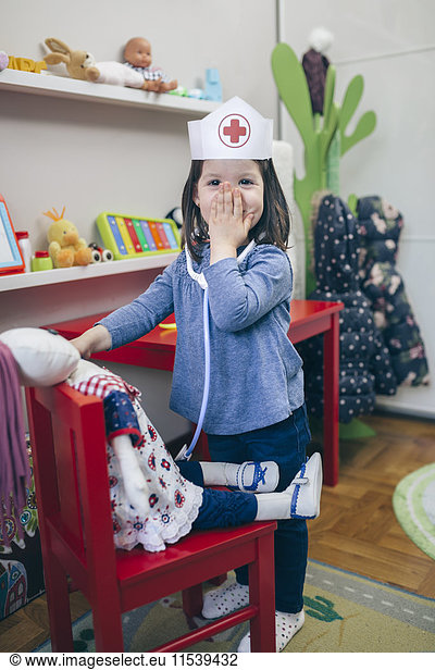 Portrait of little girl playing with medical toys covering her face with hand