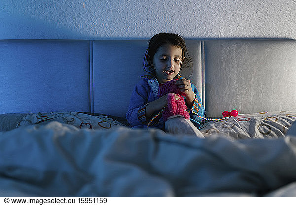 Portrait of little girl sitting on bed playing with her toy