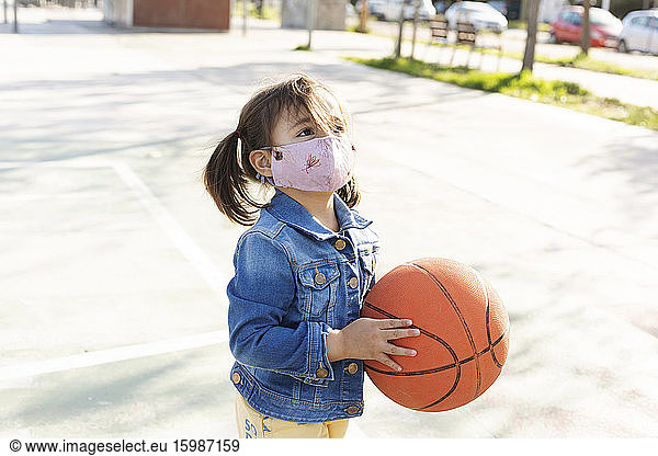 Portrait of little girl with basketball wearing protective mask