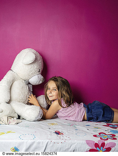 Portrait of little girl with big teddy bear in front of pink wall