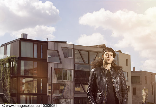 Portrait of long-haired man wearing beret and leather jacket in front of a modern building