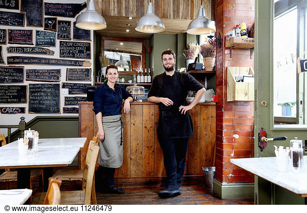 Portrait of male and female baristas leaning on counter of independent coffee shop