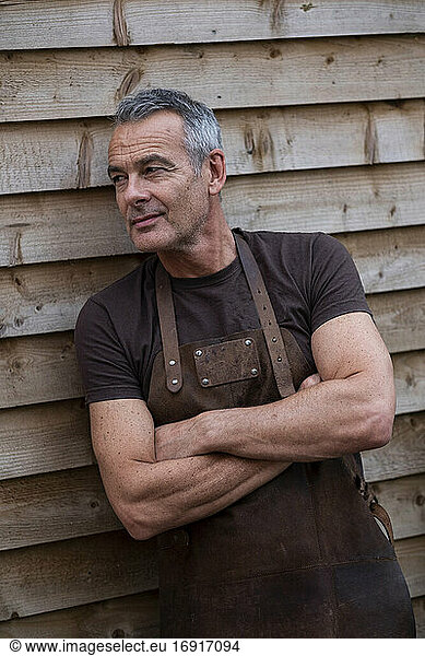 Portrait of male barista with short grey hair  leaning against wooden wall.