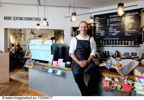 Portrait of male business owner sitting on counter of independent coffee shop