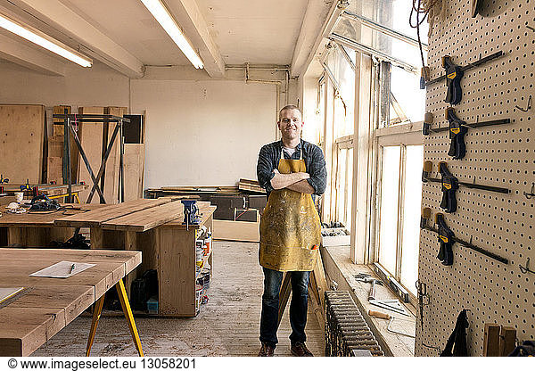Portrait of male carpenter standing by windows in workshop