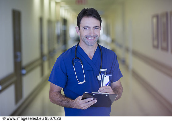 Portrait of male doctor holding clipboard in hospital corridor