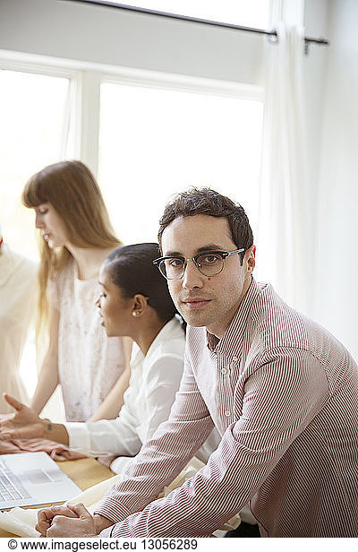 Portrait of male fashion designers with colleagues at table