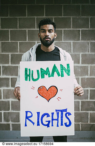 Portrait of male protestor holding human rights poster against wall