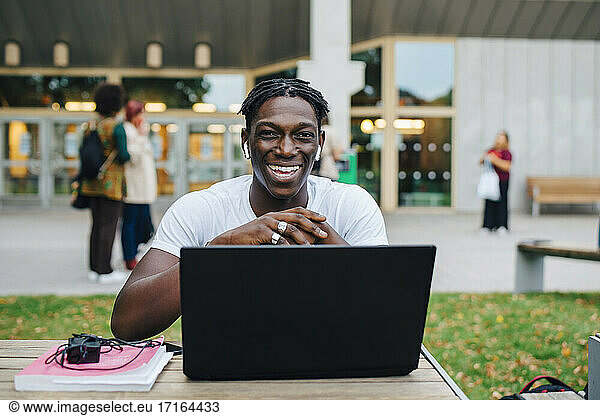Portrait of male student laughing with laptop in college campus