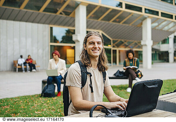 Portrait of male students e-learning through laptop in university campus