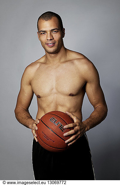 Portrait of man holding basketball while standing against gray background