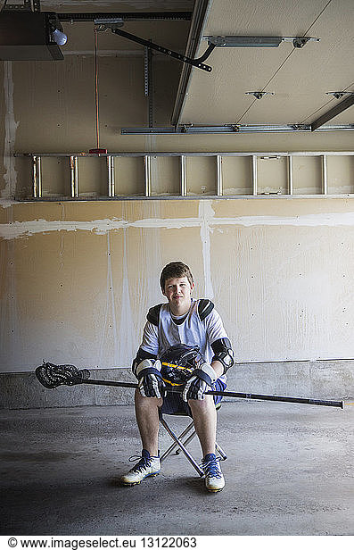 Portrait of man holding lacrosse stick and sitting on stool