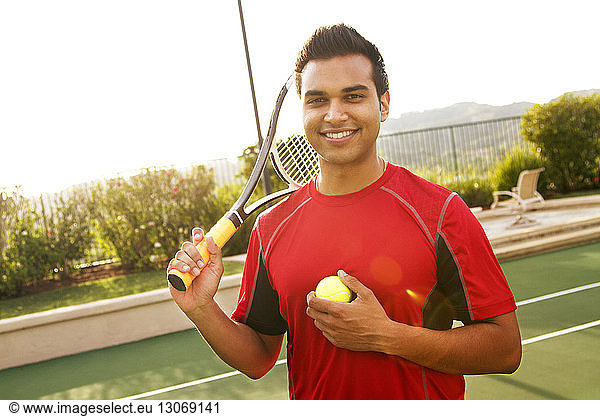 Portrait of man holding racket while standing at tennis court
