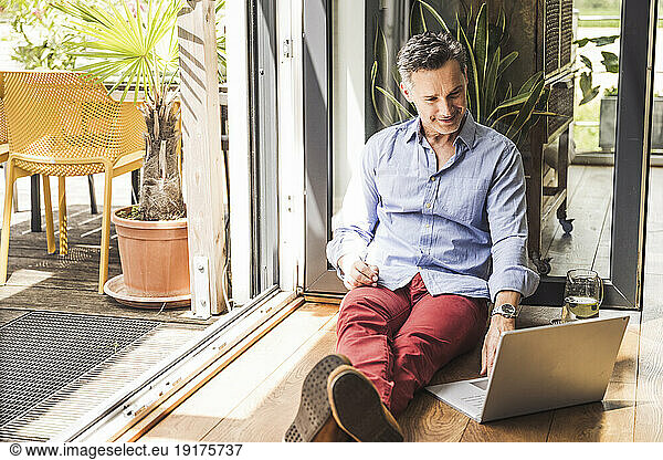 Portrait of man using laptop by open balcony