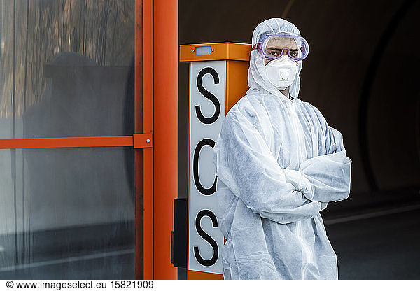 Portrait of man wearing protective clothing leaning against SOS telephone