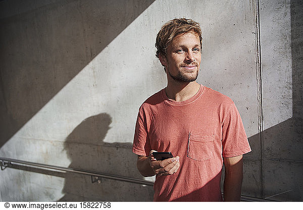 Portrait of man wearing red t-shirt holding cell phone at concrete wall