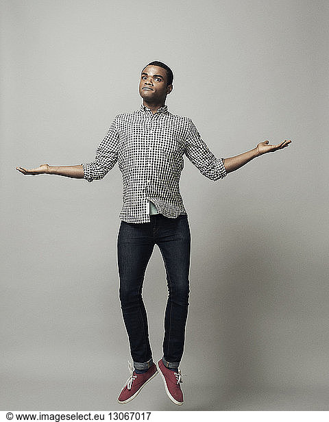 Portrait of man with arms outstretched jumping against gray background