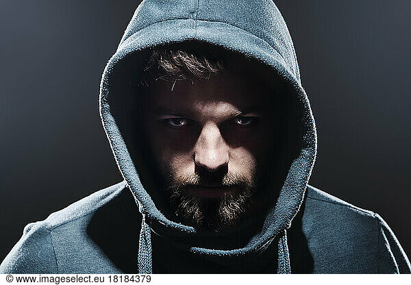 Portrait of man with hooded jacket in front of dark grey background