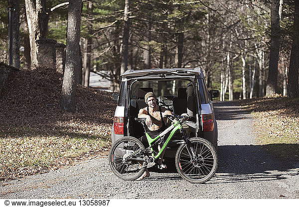 Portrait of man with mountain bike sitting on car trunk