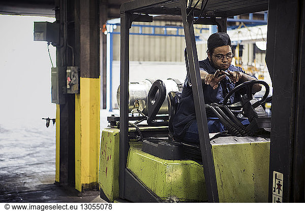 Portrait of manual worker showing peace signs while sitting in forklift at metal industry