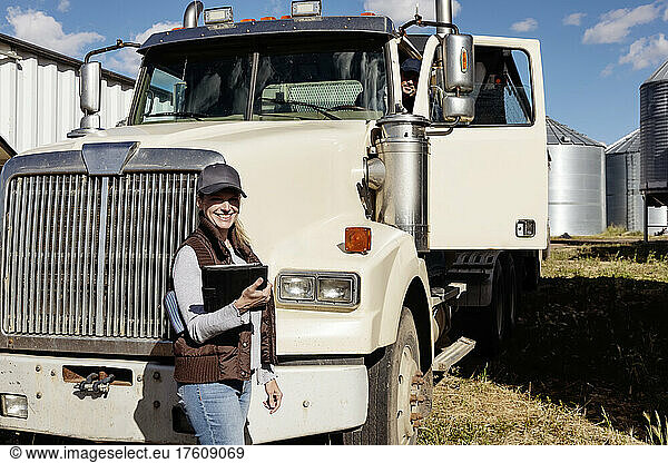 Portrait of mature couple working on their farm husband in cab of diesel truck and wife standing in front of truck holding tablet computer; Alcomdale Alberta Canada