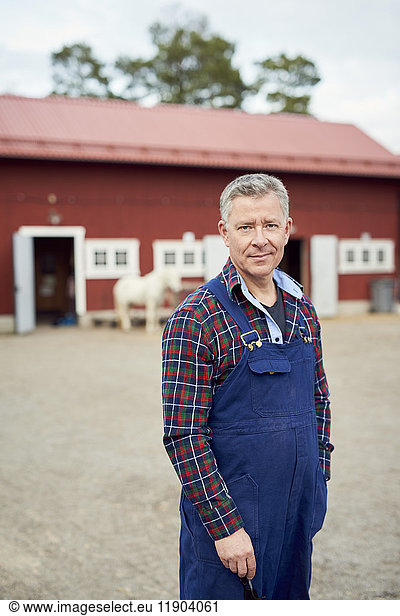 Portrait of mature farmer standing on field against barn