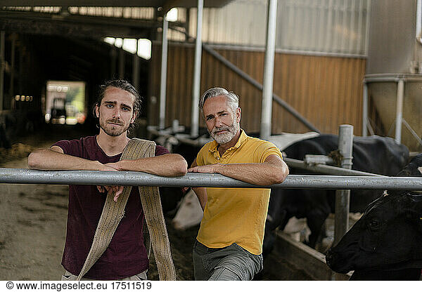 Portrait of mature farmer with adult son at cow house on a farm