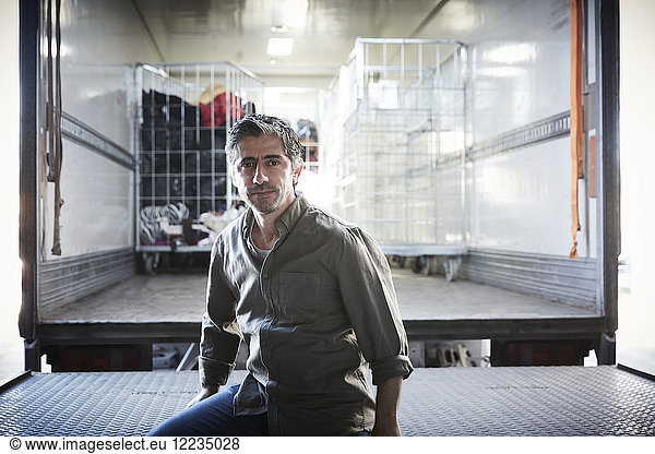 Portrait of mature male volunteer sitting against semi-truck at warehouse