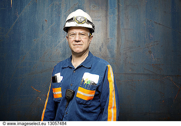 Portrait of mature male worker standing against metal wall
