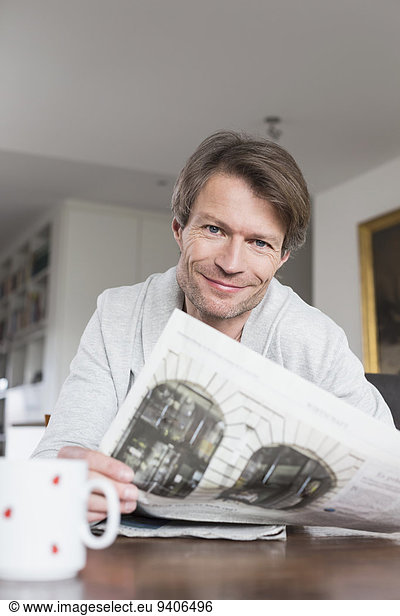 Portrait of mature man having coffee and reading newspaper  smiling
